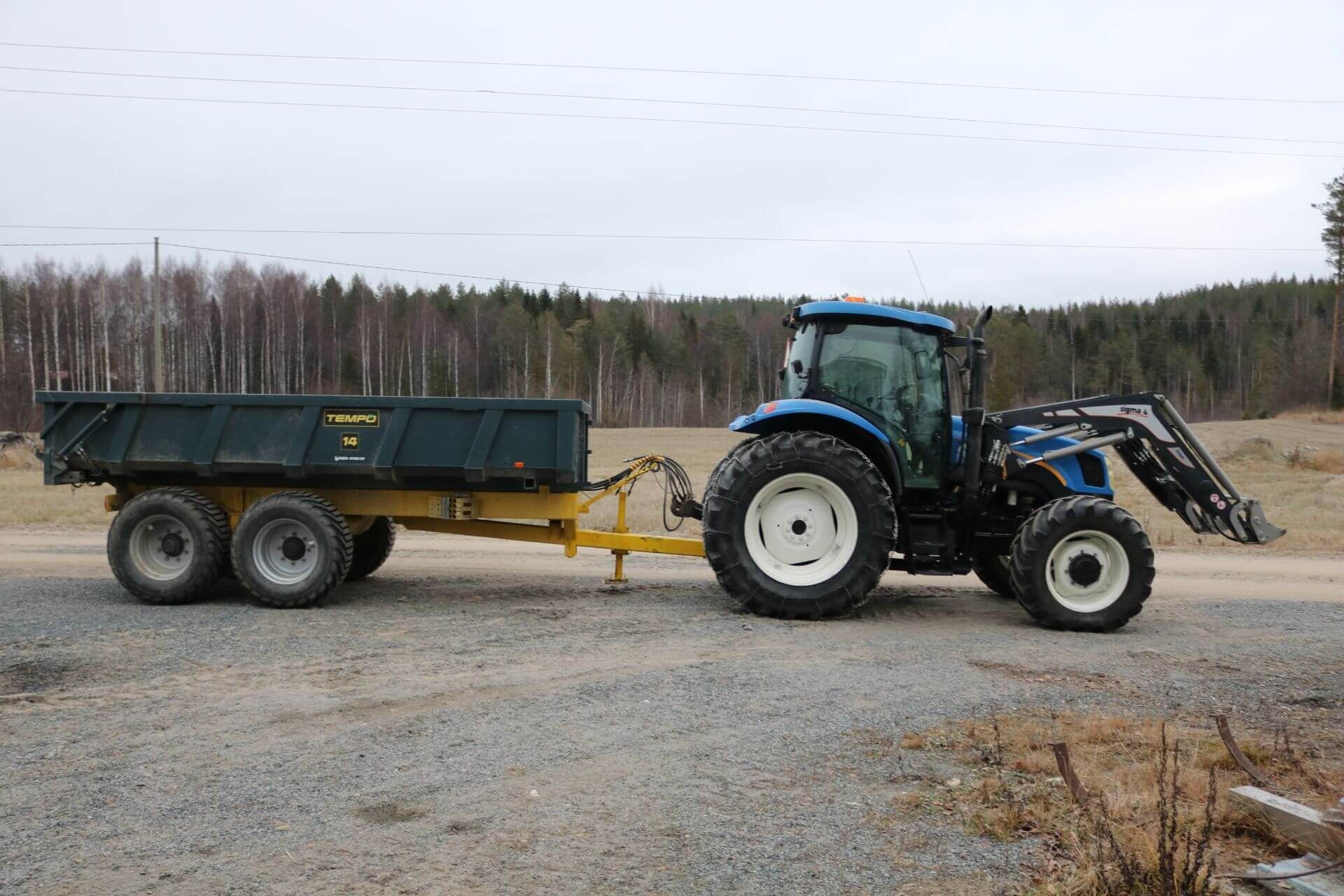 Sininen traktori ja sen metallikaukaloinen peräkärry.